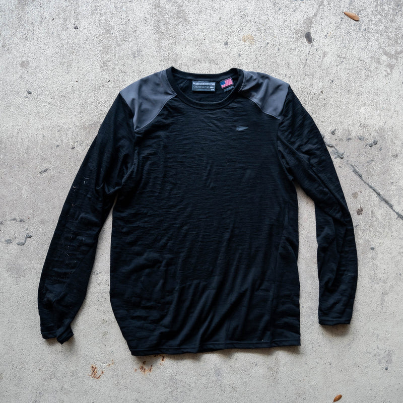 Men’s Commando Long Sleeve - Merino Wool in black, featuring reinforced shoulders and a classic commando sweater design, laid flat on a concrete surface.
