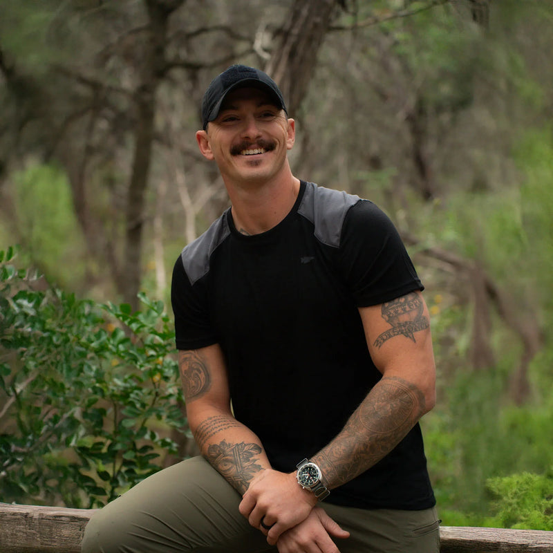 Man in GORUCK athletic gear with tattoos, smiling outdoors in a forest setting