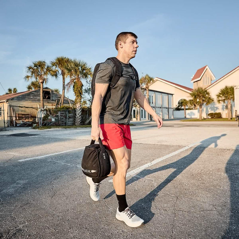 Man rucking outdoors with GORUCK backpack and gym bag, wearing athletic gear