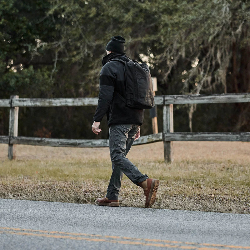 Man rucking with GORUCK backpack outdoors near wooden fence, wearing outdoor gear