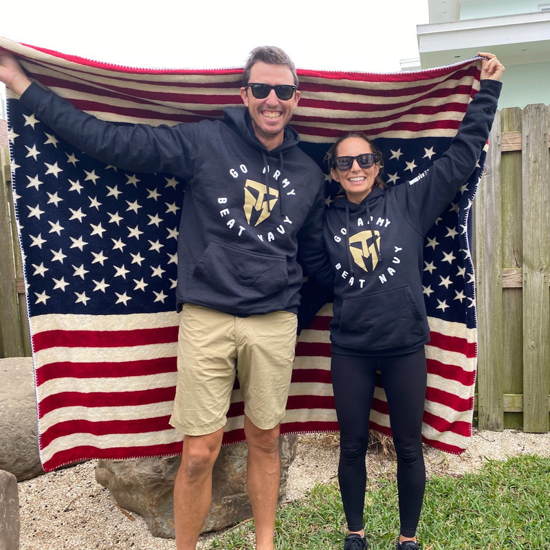 Two people wearing "Go Army Beat Navy" hoodies and Men’s Simple Shorts - Lightweight ToughDry® hold an American flag blanket behind them, smiling outdoors.