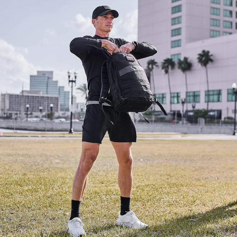Man in GORUCK performance tee and shorts with backpack outdoors in urban park