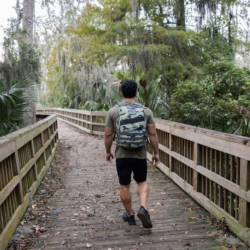 Man rucking in forest with GORUCK camo backpack on wooden trail bridge