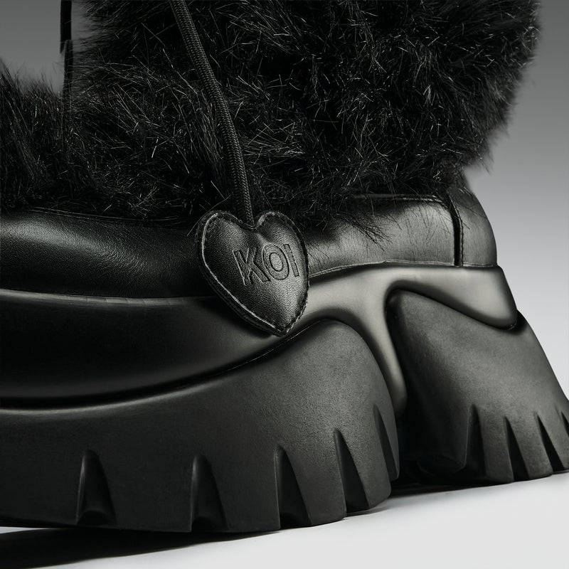 Black snow boot with thick fur lining and a heart-shaped brand logo on a neutral background