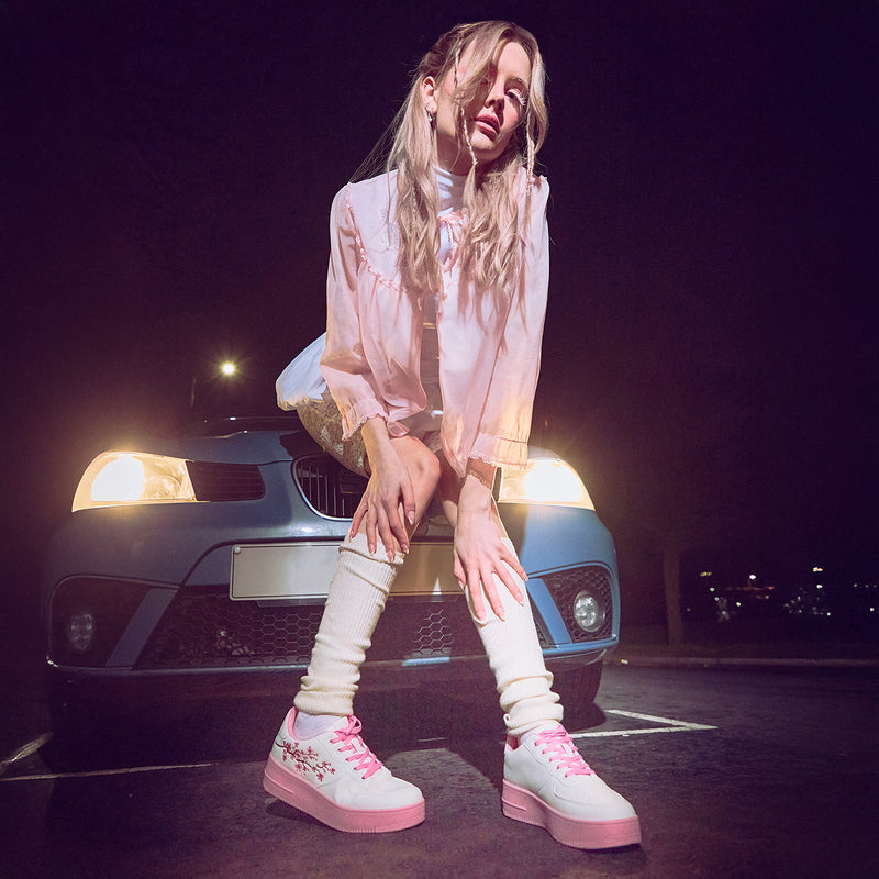 A pair of white platform trainers with pink floral embroidery on the top and a pink sole - Model View