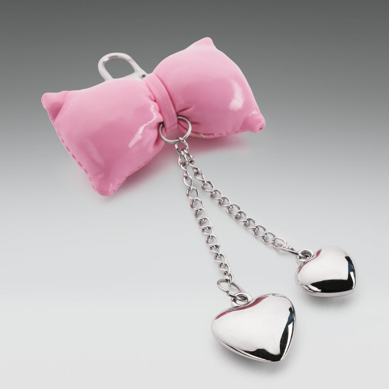 Pink bow-shaped keychain with silver chain and heart-shaped pendants on a gray background