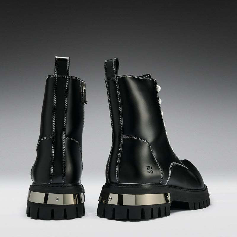 Black leather boots with metallic heel accents on a gradient gray background