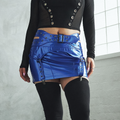Person wearing a black crop top and blue metallic skirt with a belt, standing against a light gray wall.