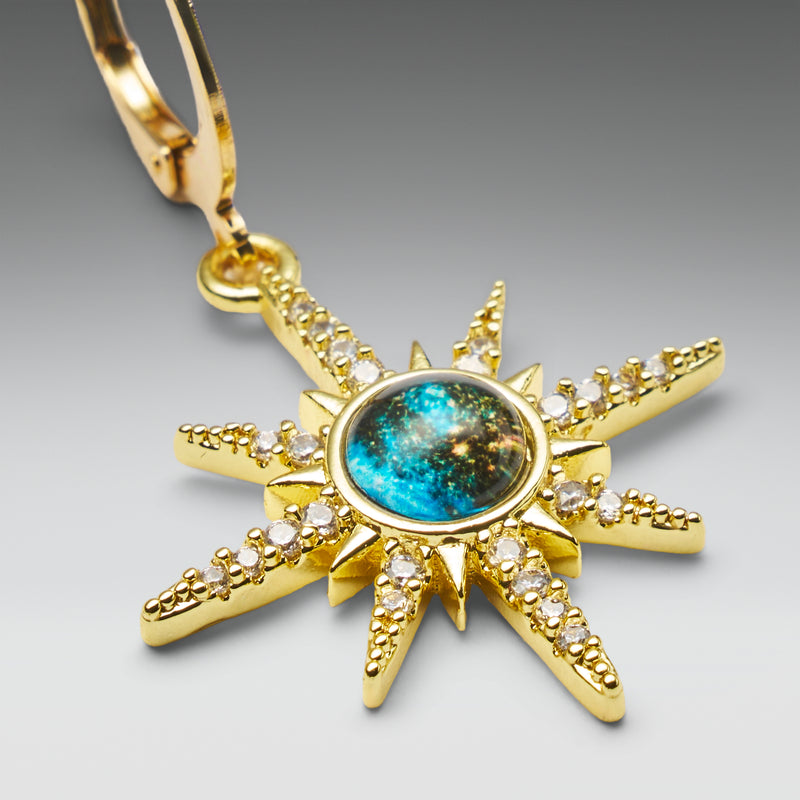 Gold sun-shaped pendant with a blue gemstone on a gray background