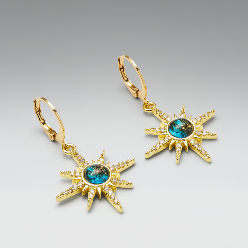 Gold sun-shaped earrings with gemstones on a gray background