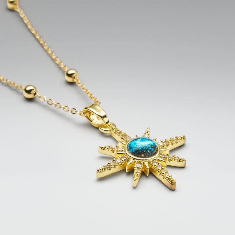 Gold necklace with a star-shaped pendant featuring a blue gemstone on a gray background