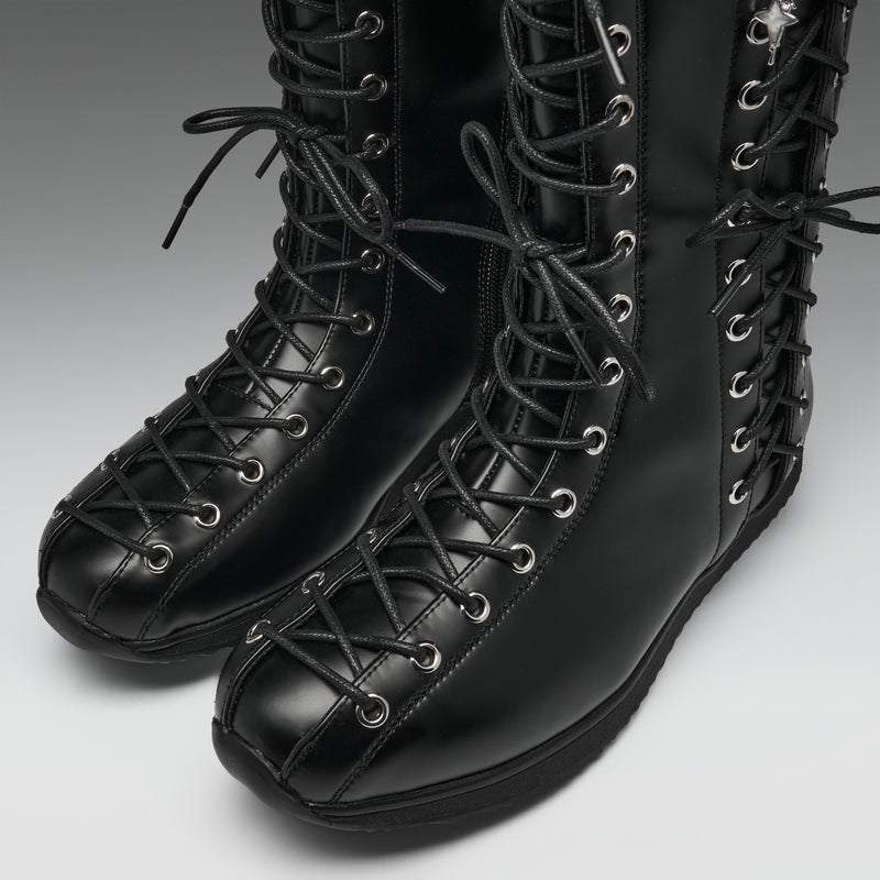 A pair of black leather lace-up boots with silver metal eyelets, shown on a neutral gray background.