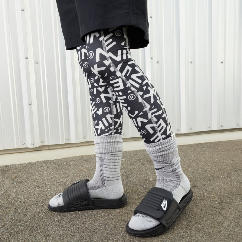 Women’s black Nike slide sandals worn with patterned socks and black shorts