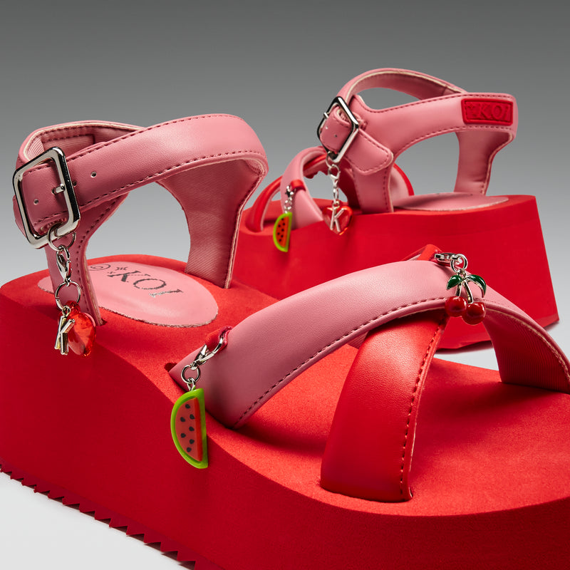 Pink sandals with fruit charms on a red platform against a gray background