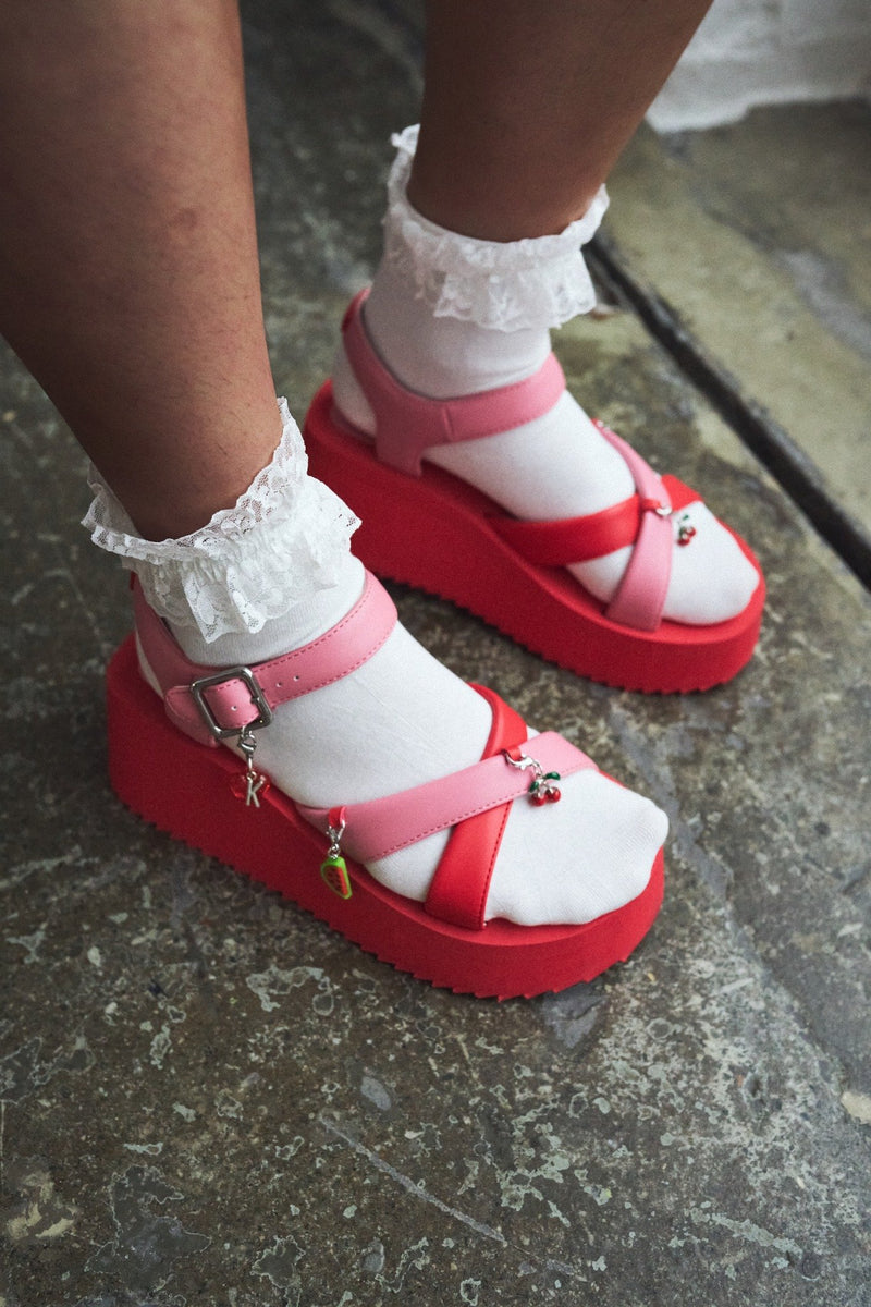 Red platform sandals with white soles worn on a concrete surface
