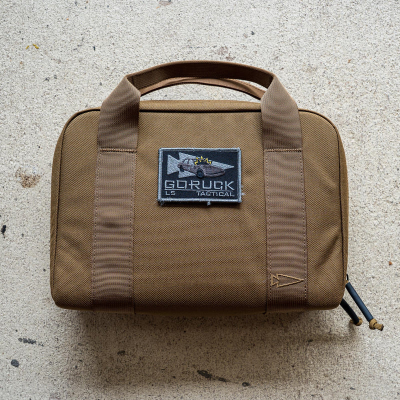 The brown Pistol Rug with handles and a "GORUCK Tactical" patch sits on a light textured surface—ideal as a modular pistol case or magazine pouch.