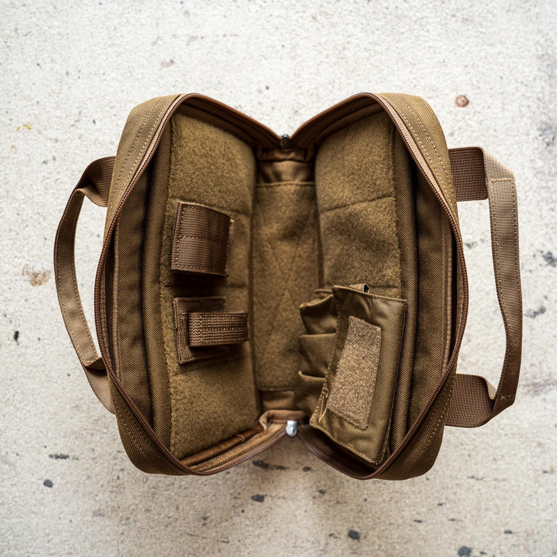 A brown Pistol Rug with compartments and straps lies open on a light, speckled surface.