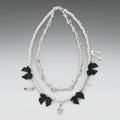 Necklace with black bow charms and silver treble clef on a gray background