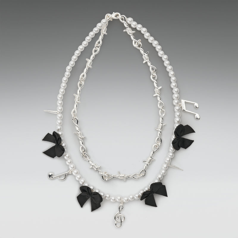 Necklace with black bow charms and silver treble clef on a gray background