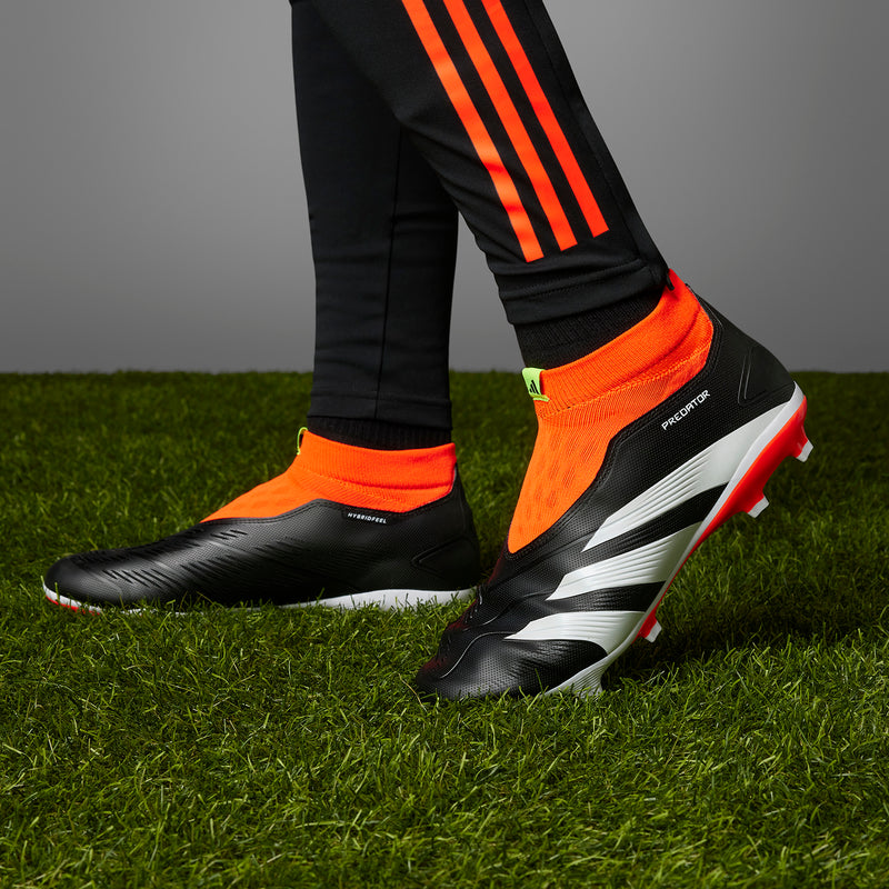 Men's firm-ground soccer boots, black with white stripes and orange-red accents on grass