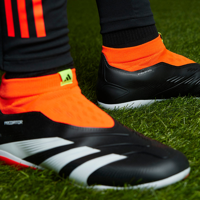 Close-up of black soccer boot with orange-red sock collar and white stripe detailing
