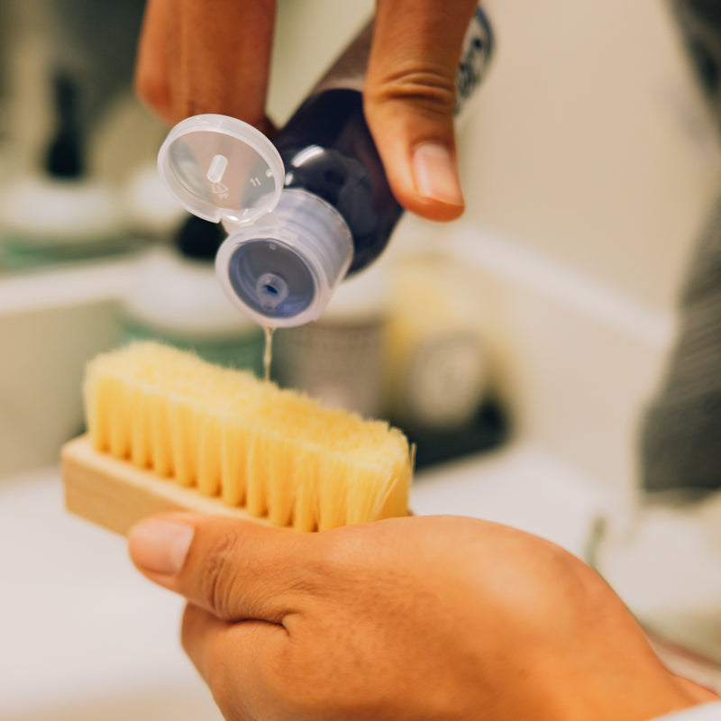 Shoe cleaner bottle cap open above a bristle brush for applying cleaner.