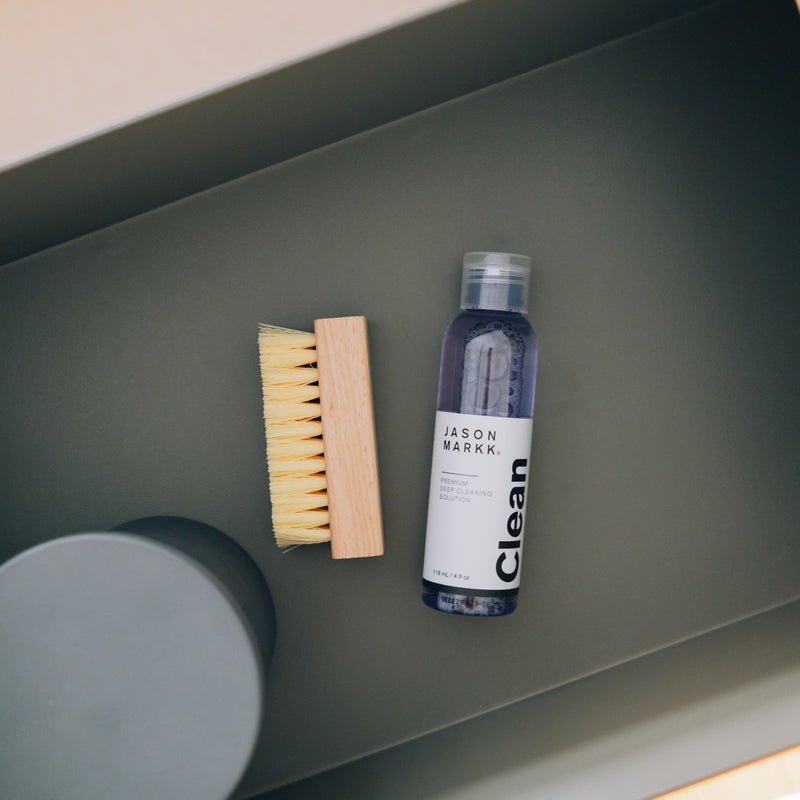 Shoe cleaner bottle with bristle brush and foam cleaning pad on shelf.