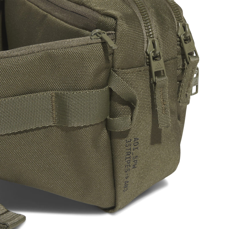 Olive crossbody bag side view with zippers, stitched panels, and webbing pocket