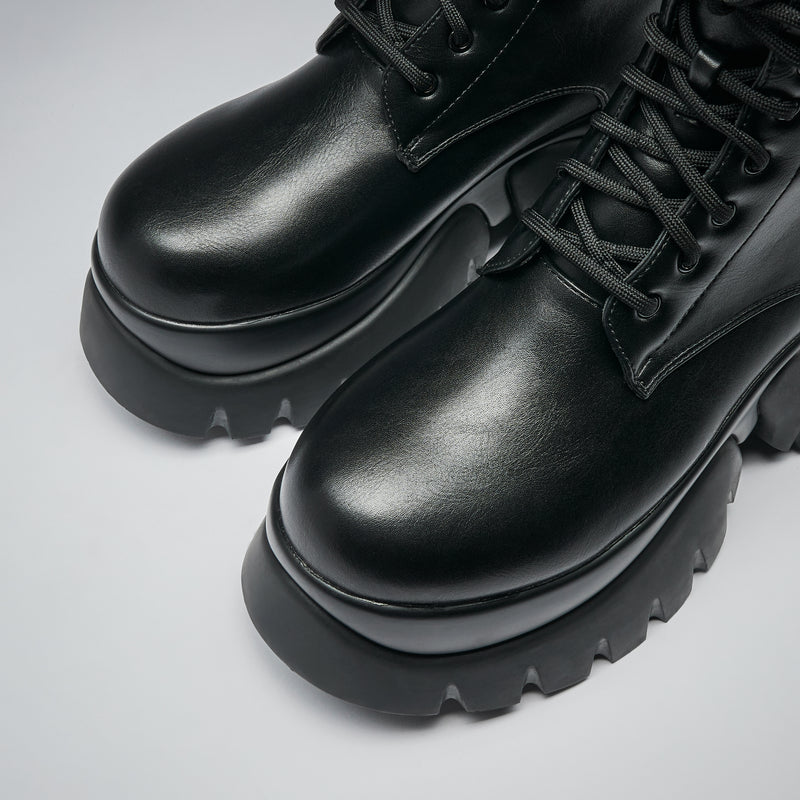 Pair of black leather boots with thick soles on a light gray background