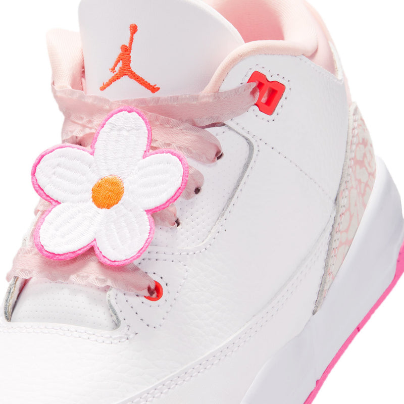 Kids sneaker close-up: white leather upper with pink flower applique and orange Jumpman on tongue