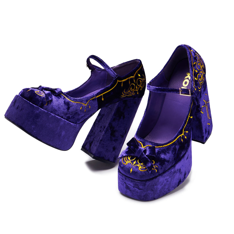 A purple velvet platform heel with gold embroidery, including a cross and floral details, with a chunky heel and ankle strap - walking 3/4 view