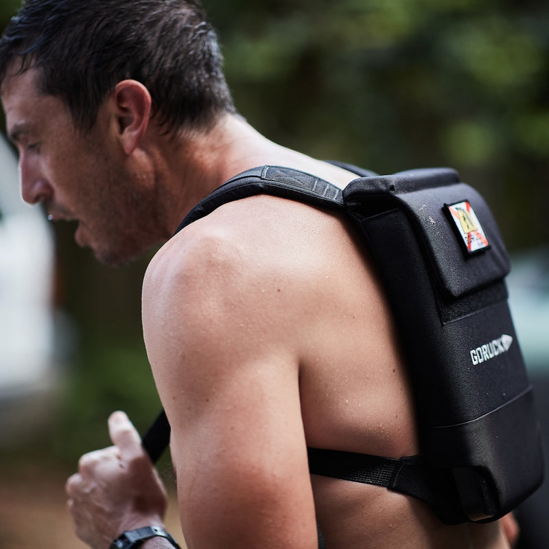 A man outdoors wearing the Ruck Plate Carrier 3.0 weighted backpack, with enhanced lumbar support visible on the strap.