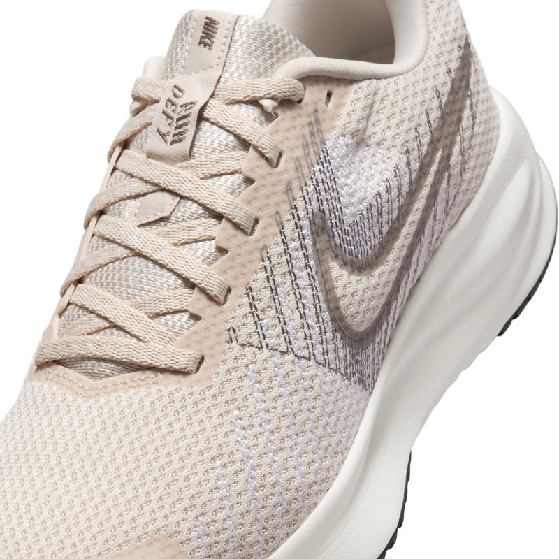 Light beige running shoe close-up with laces, knit texture, and side swoosh detail.