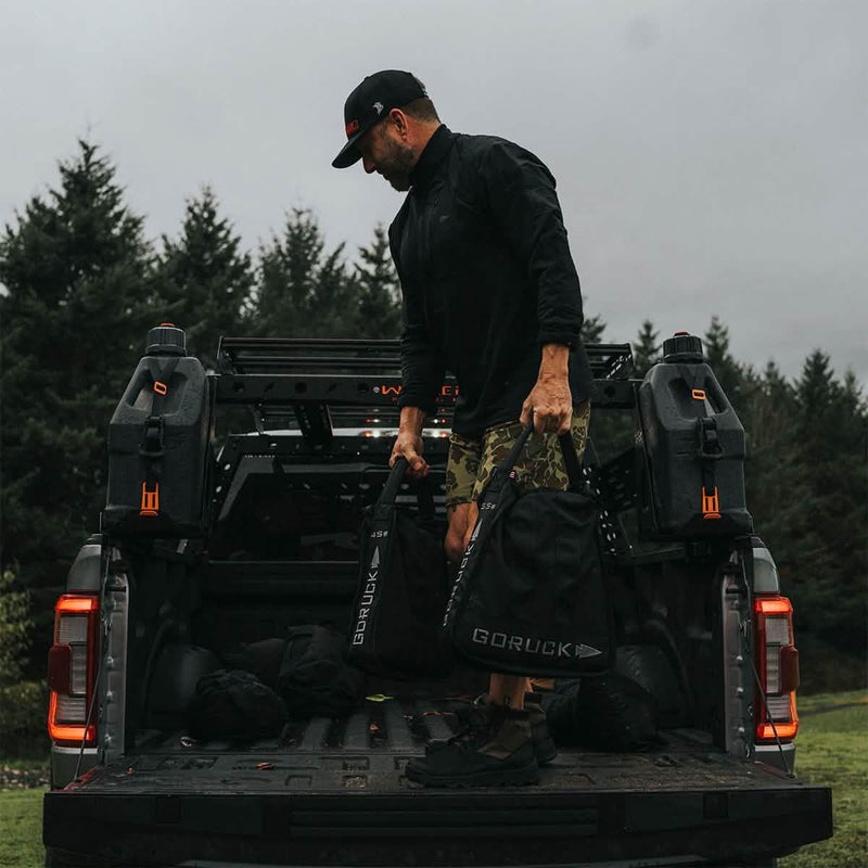Man loading GORUCK sandbags and gear onto truck bed outdoors, featuring rugged rucking equipment.