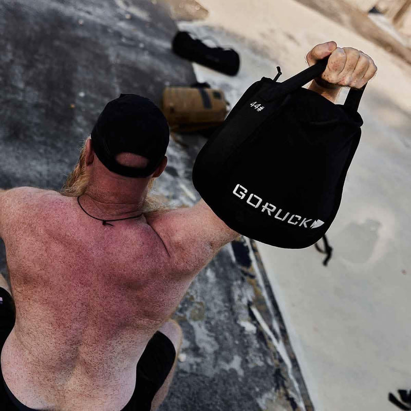 Man lifting GORUCK 44 lb sandbag outdoors, showcasing durable rucking gear
