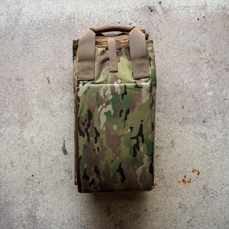 A folded camouflage-patterned Shooting Mat rests on a textured concrete surface.