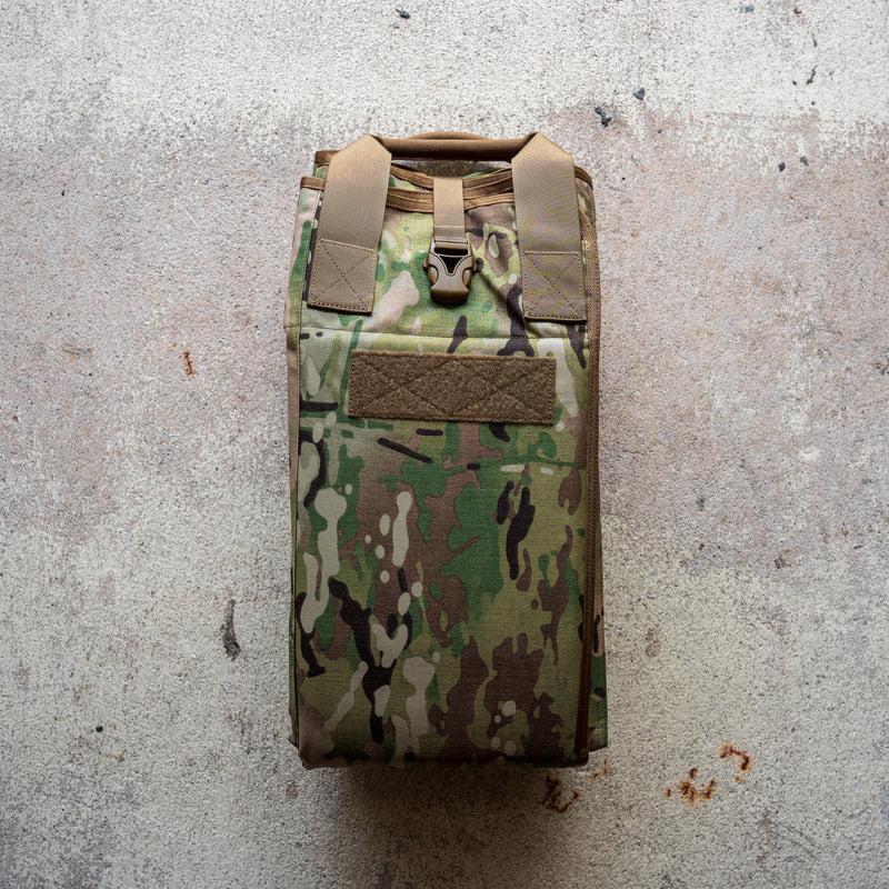 A folded camouflage Shooting Mat with tan straps rests on a textured concrete surface.