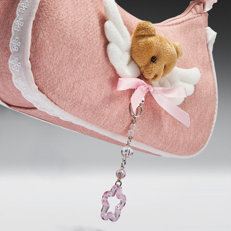 Pink handbag with a teddy bear angel keychain on a gray background