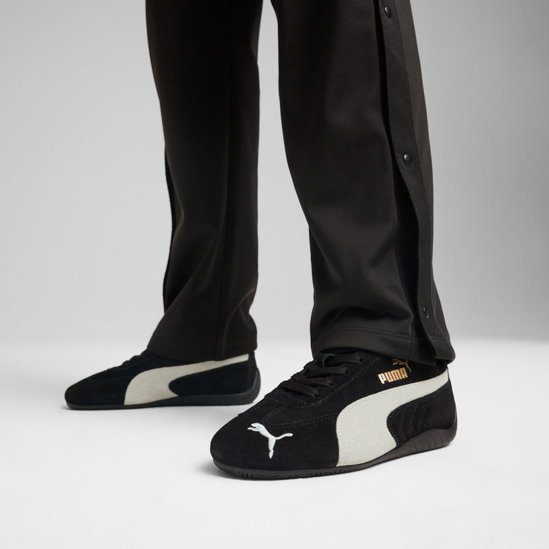Youth Puma sneakers worn with black pants, black uppers with white stripe and logo