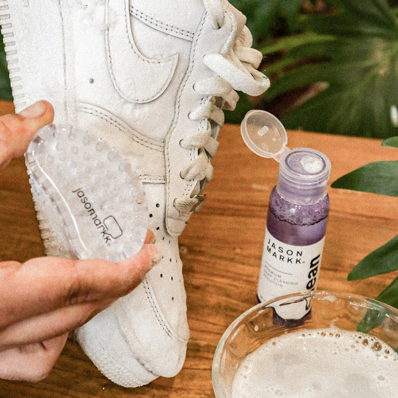 Shoe care kit cleaning a white sneaker with brush and cleaner bottle