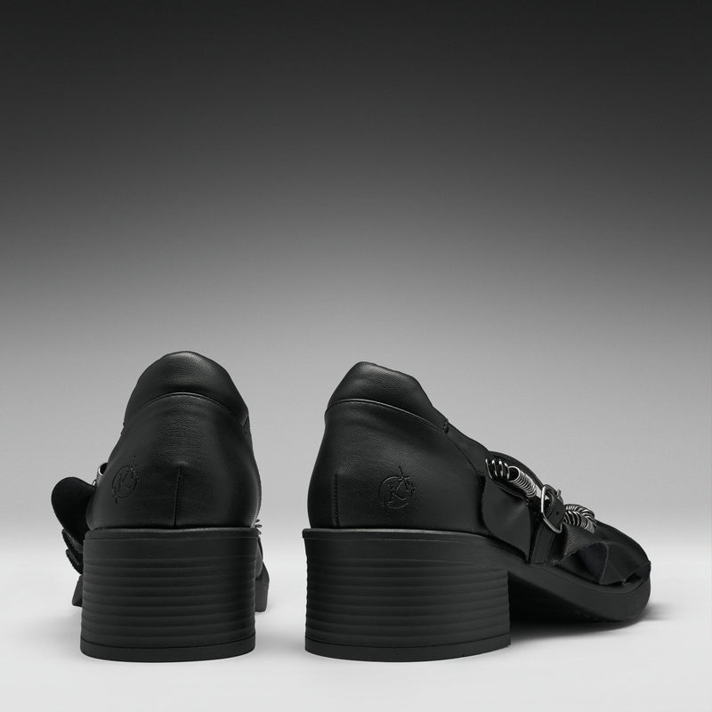 A pair of black leather high-heeled sandals shown from the back, featuring chunky stacked block heels and decorative side straps, set against a dark gray gradient background.