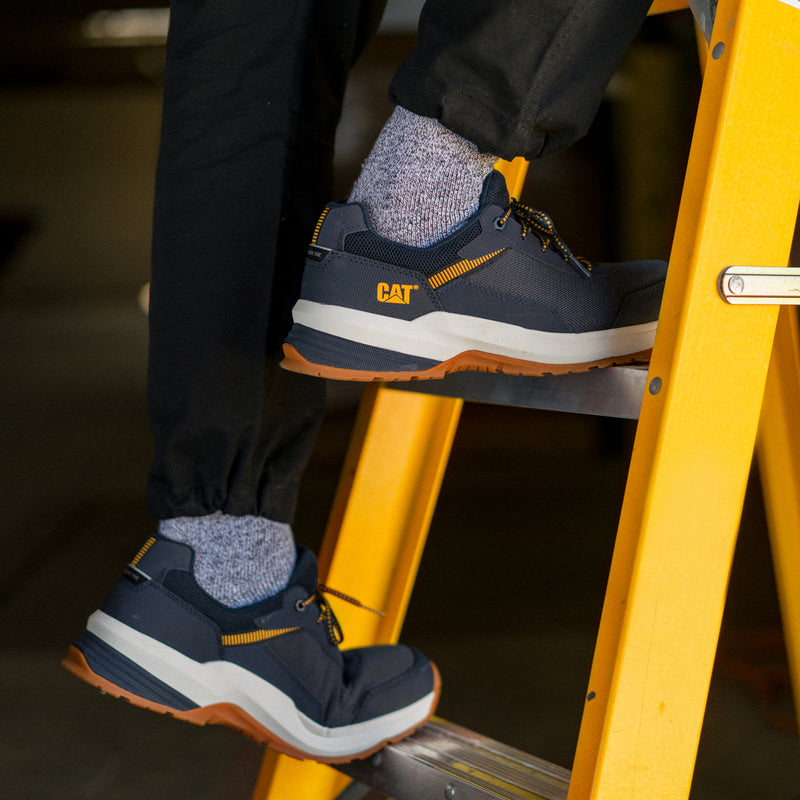 Men's CAT safety sneaker with navy upper, white midsole, yellow laces, gum outsole