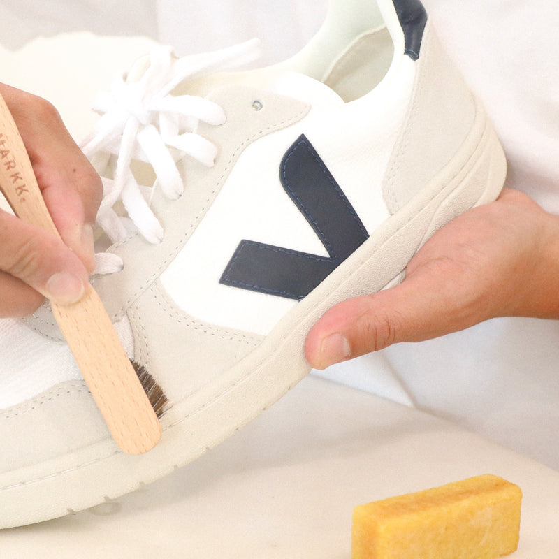 White suede sneaker being brushed with a wooden brush and yellow eraser