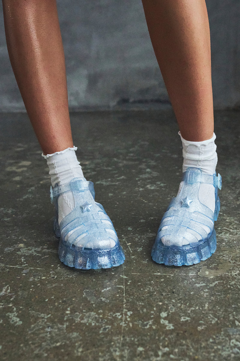 Blue sandals worn with white socks on a dark floor.
