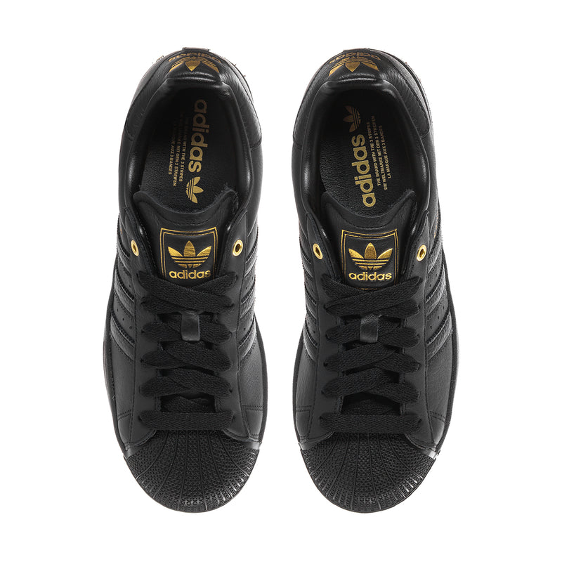Men's black Adidas sneakers, inside view of tongue and heel with gold logo detail.