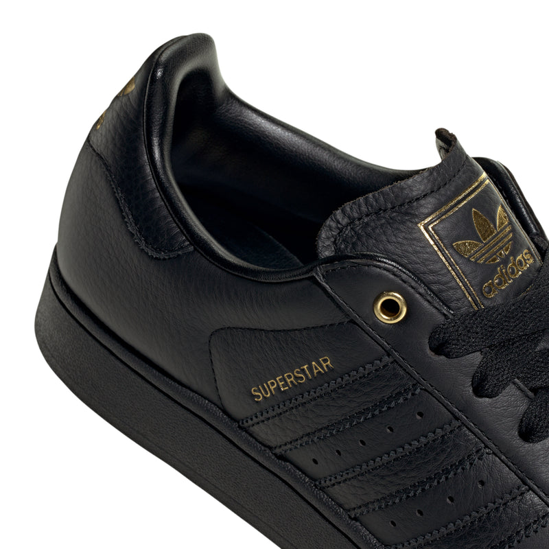 Men's black leather low-top sneakers, Superstar logo patch and gold lace eyelet.