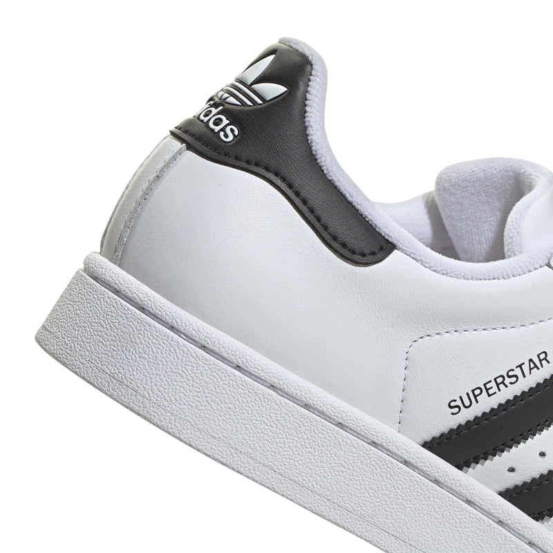Close-up of women's white and black sneaker with SUPSERSTAR side text and white midsole