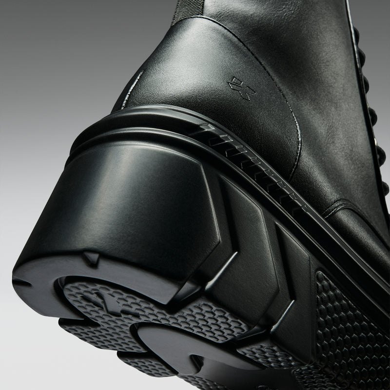 Close-up of a black boot with a textured sole on a gray background