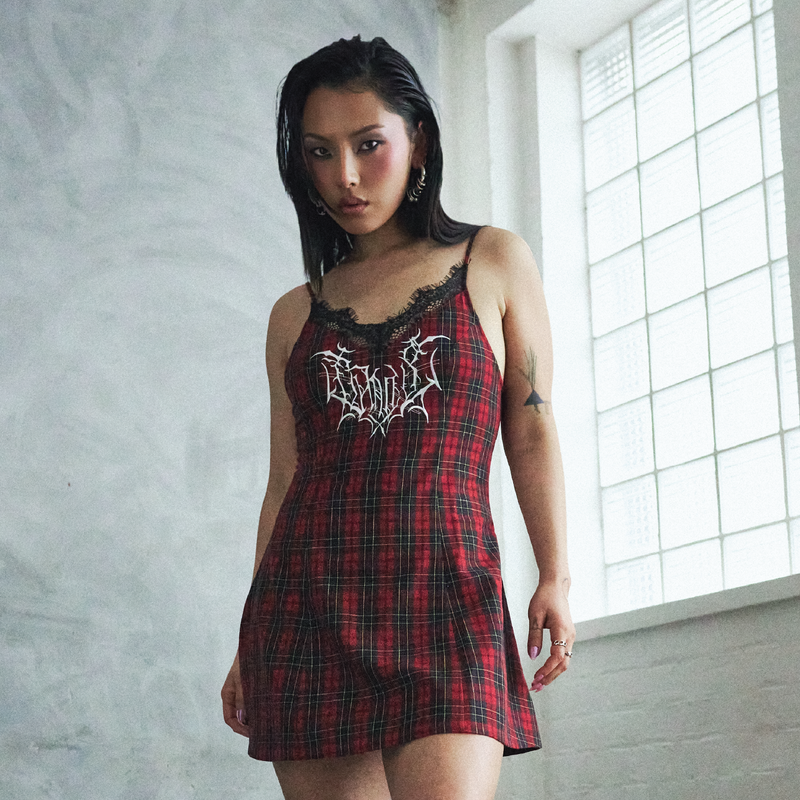Woman wearing a red plaid dress with lace details in a room with a window.