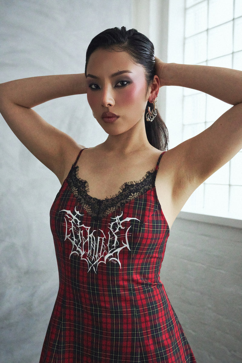 Woman wearing a red plaid dress with black lace details in a studio setting.